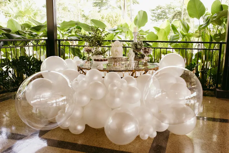 Elegant white and clear balloon installation around a dessert table on a leafy terrace