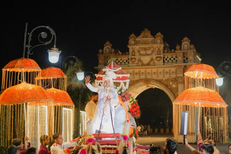 Groom's night-time procession with glowing orange parasols in front of an illuminated palace gateway