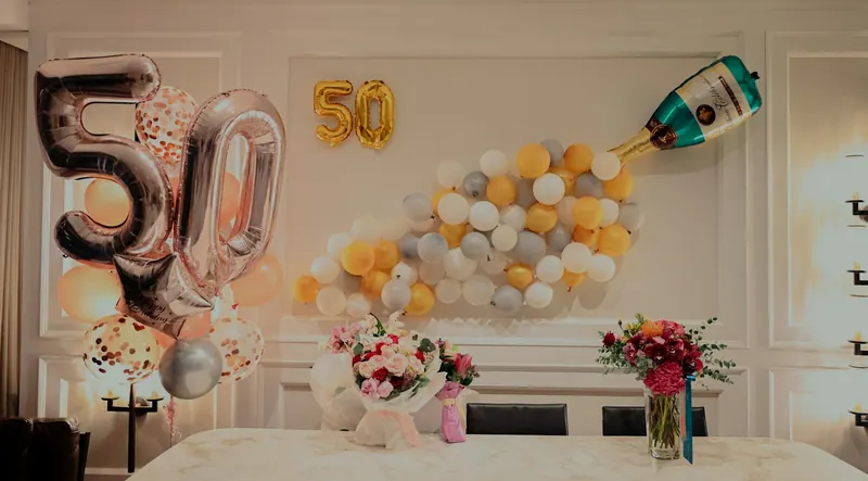 50th birthday setup with foil number balloons, a champagne balloon wall and flowers