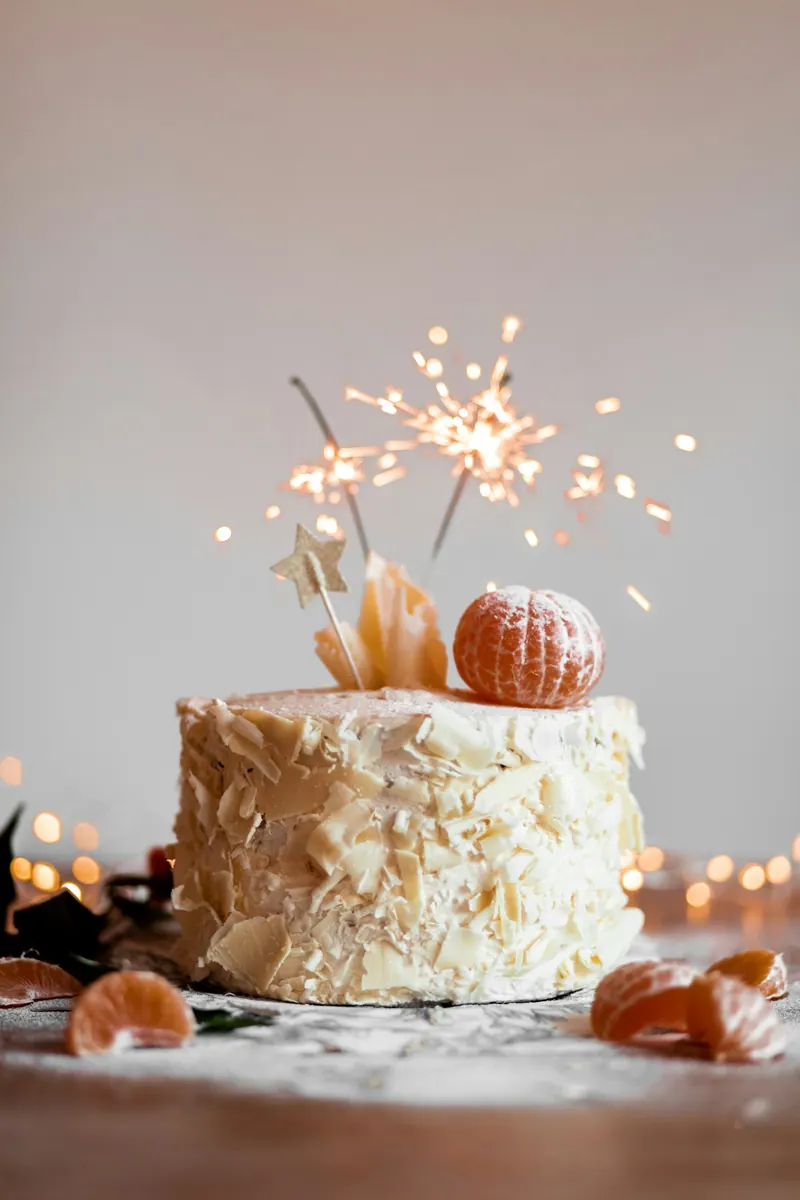 Cream birthday cake topped with a lit sparkler and tangerines