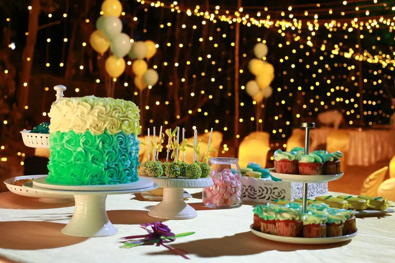 Birthday cake and cupcake dessert table under glowing fairy lights and balloons