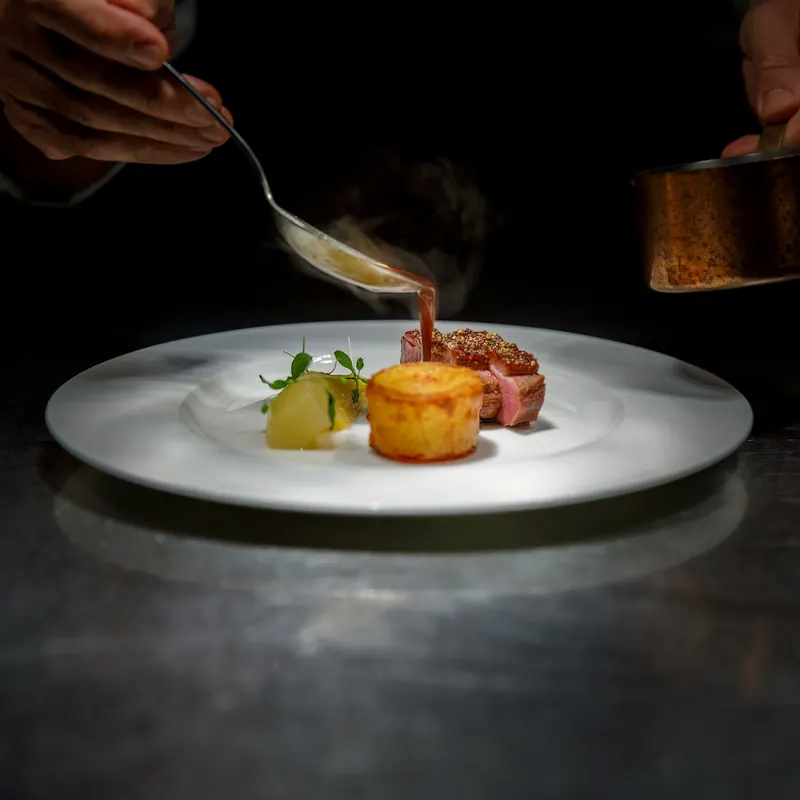 Chef spooning sauce onto a finely plated main course