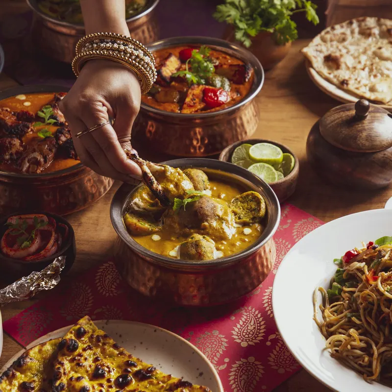 Hand serving from hammered copper handis of Indian curries with naan and lime