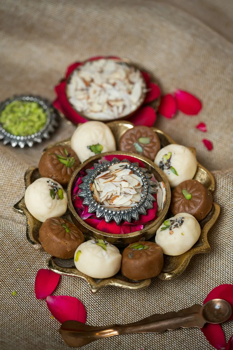 Brass platter of Indian sweets with rose petals and pistachio