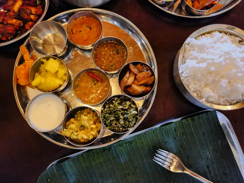 Steel thali with assorted Indian curries and sides beside rice and a banana leaf