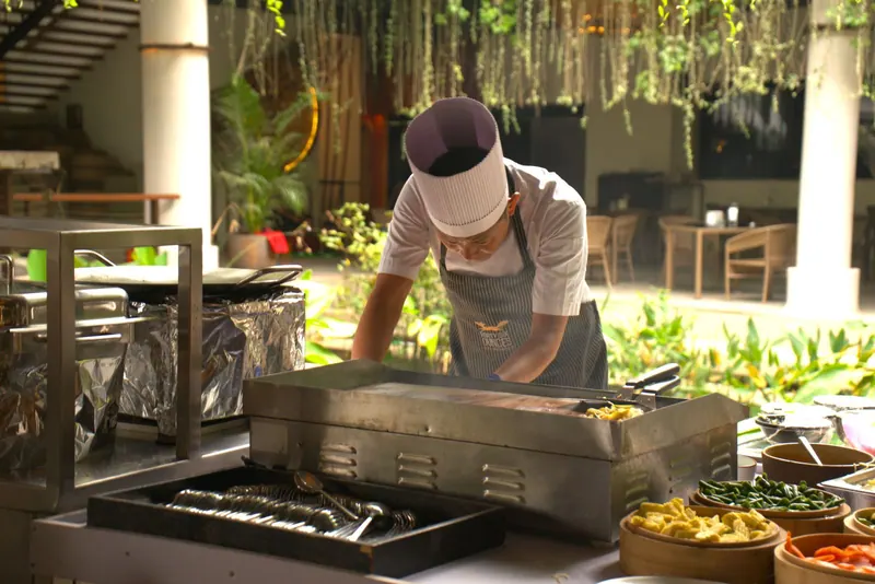 Chef cooking at an outdoor live grill counter beside bowls of fresh ingredients