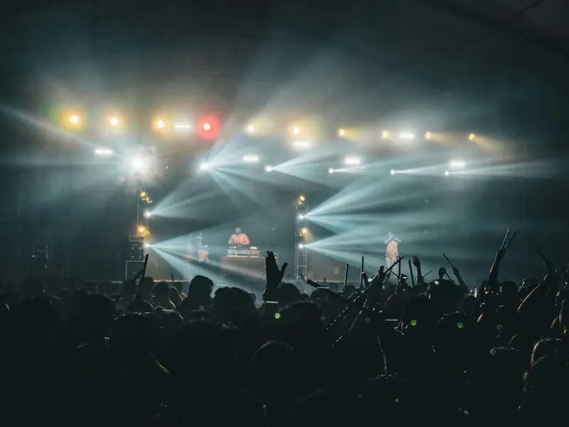 Crowd with raised hands before a stage lit by sweeping light beams