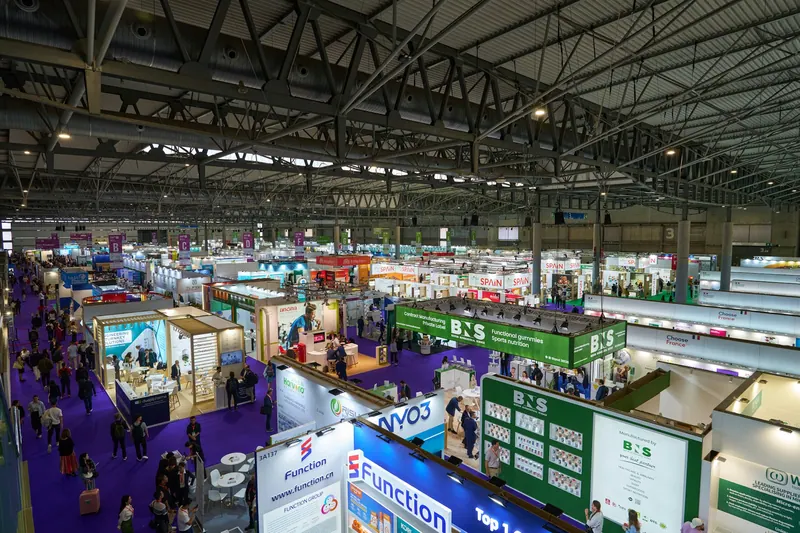 High view of a busy trade exhibition hall lined with branded booths and visitors