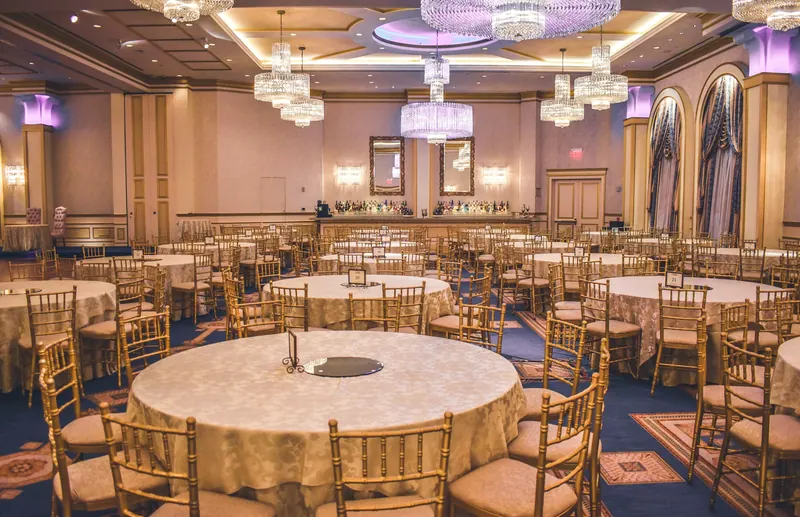Grand banquet hall set with round tables, gold chairs and chandeliers before a gala dinner