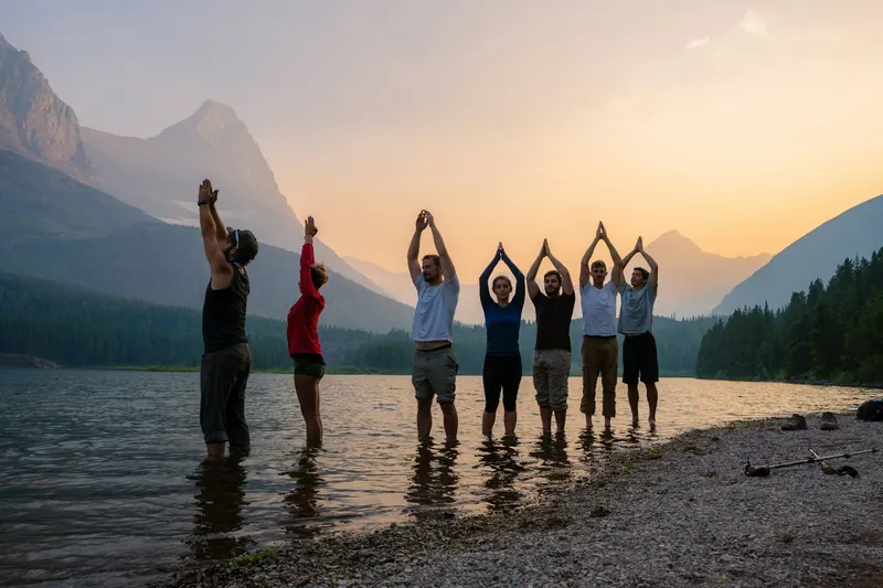 Team standing in a lake at sunset with arms raised during an outdoor offsite