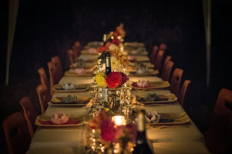 Long candlelit banquet table with dahlia centrepieces and folded napkins in a dark, intimate room