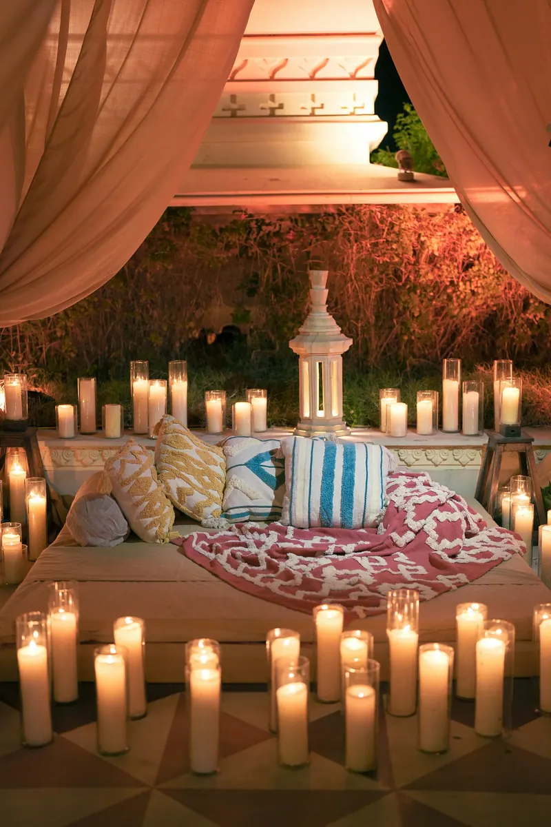Low lounge seating with cushions under blush drapes, surrounded by dozens of pillar candles