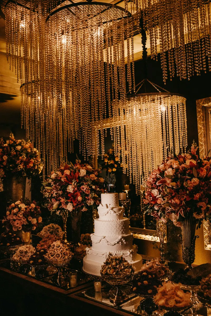Tiered white wedding cake beneath crystal-strand chandeliers, flanked by rose arrangements