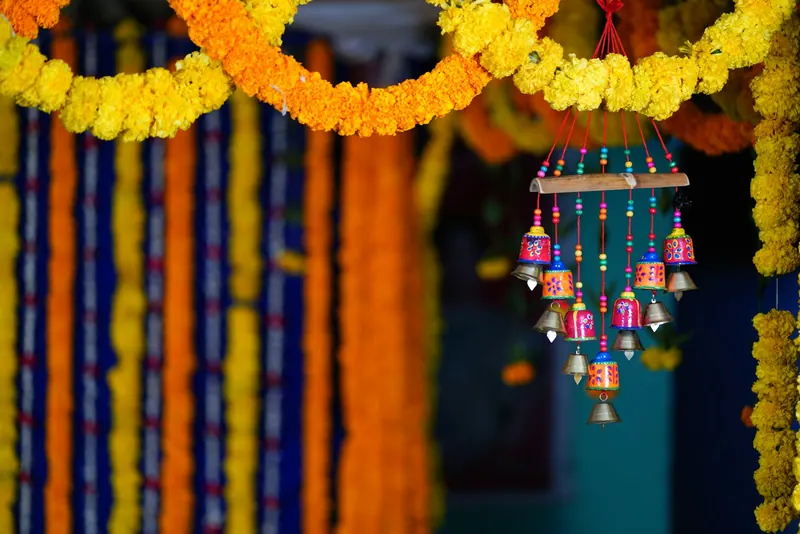 Strings of orange and yellow marigold garlands with a hanging bell ornament