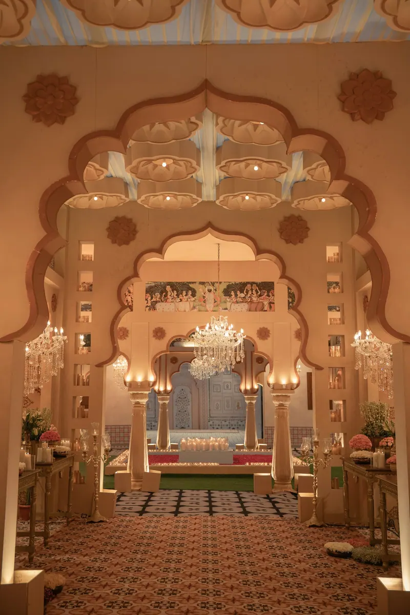 Carved Rajasthani-style arches lit by chandeliers framing a decorated entrance passage