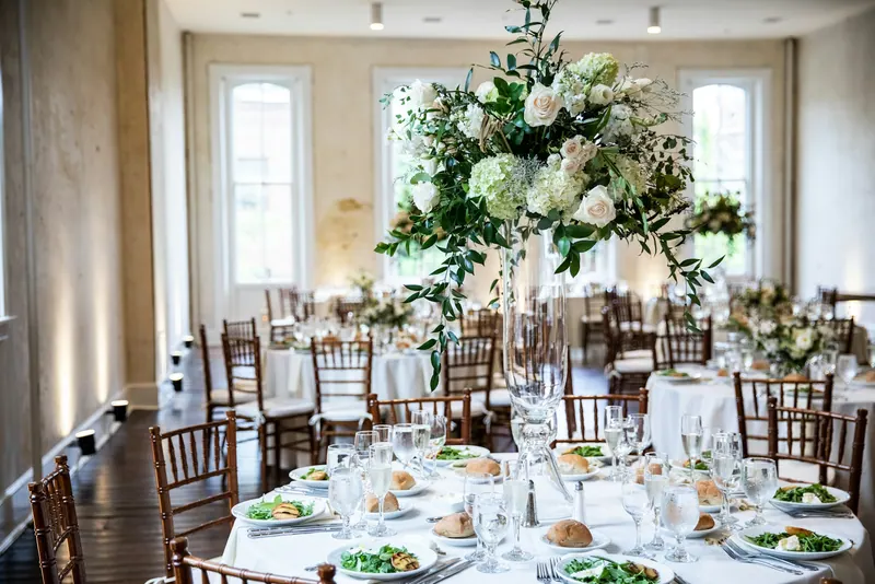 Tall white rose and hydrangea centrepiece above round tables set for a reception