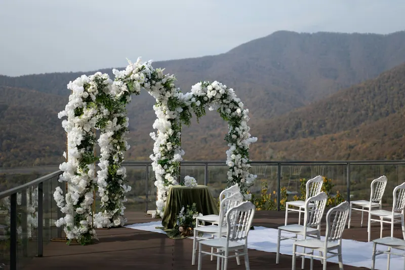 White floral arch and chairs on a hilltop terrace overlooking forested mountains