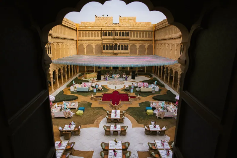 View through a carved arch into a golden sandstone palace courtyard set for a wedding celebration