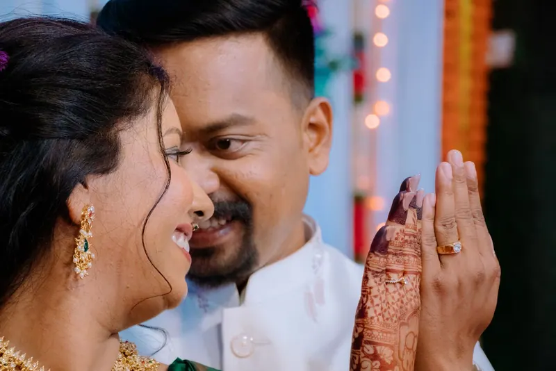 Smiling couple leaning together as the bride shows her hennaed hand and engagement ring