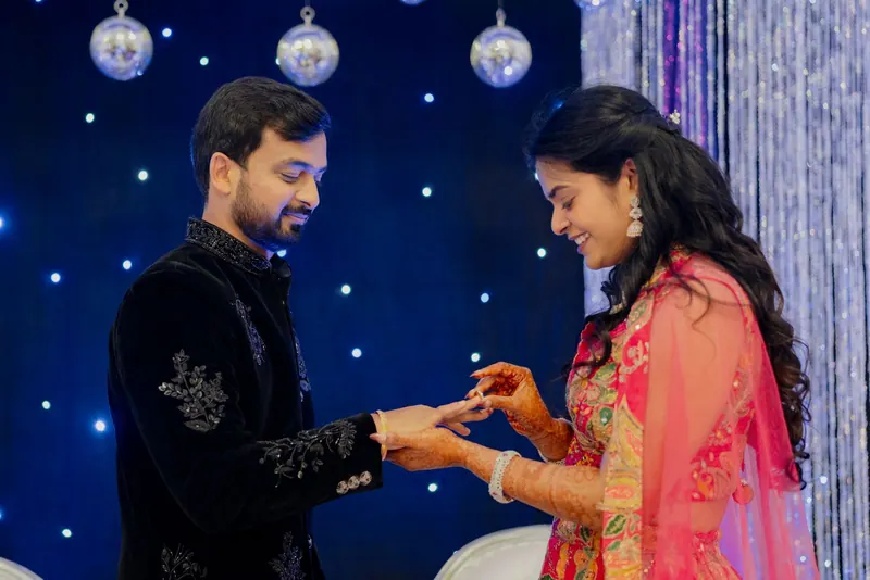 Couple exchanging rings on stage against a starry blue backdrop with hanging lights