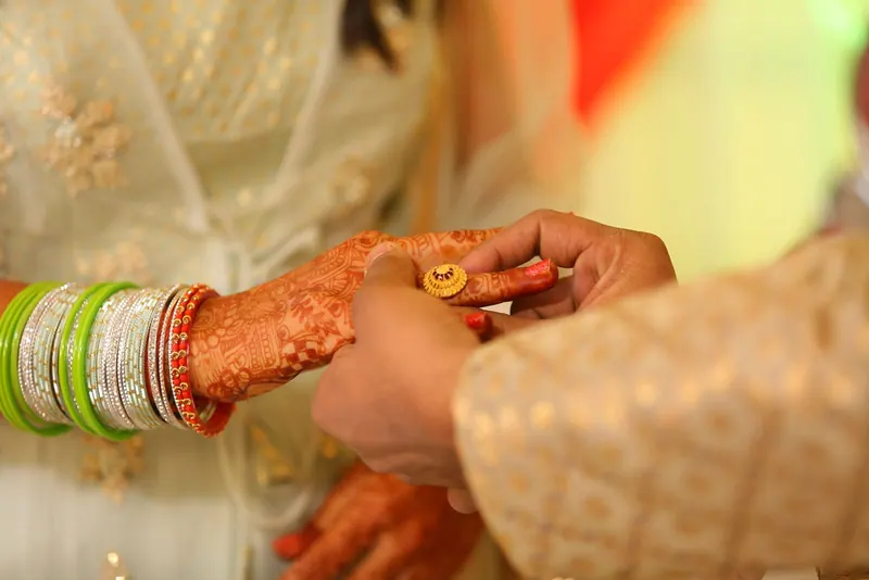 Groom slipping an engagement ring onto the bride's hennaed finger
