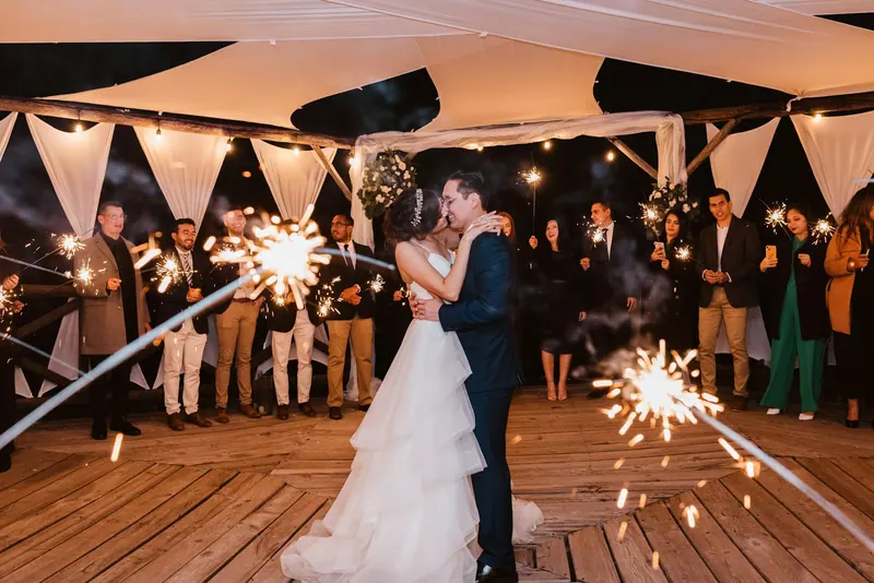 Couple sharing a first dance as guests hold sparklers under a draped pavilion