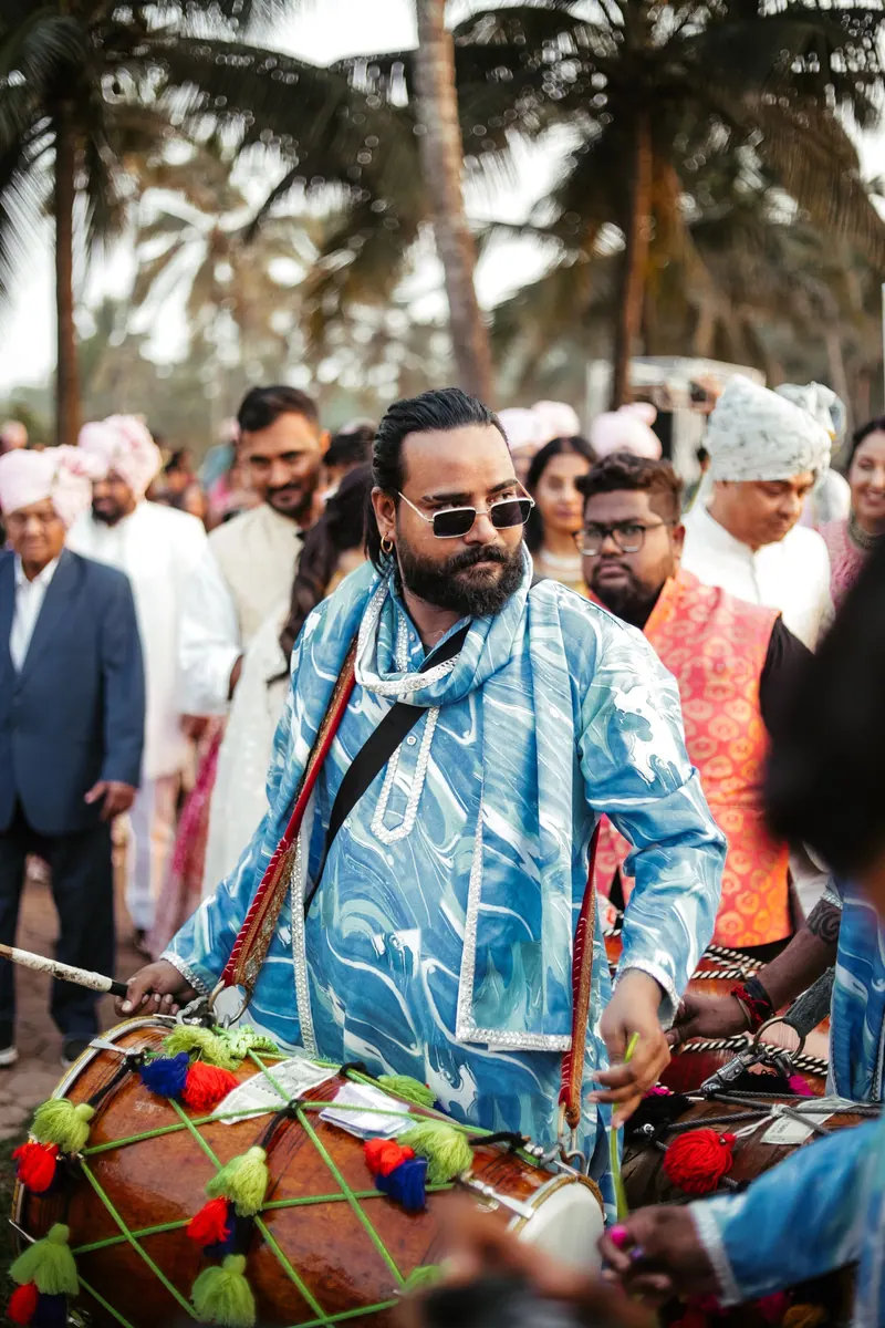 Dhol player drumming through a lively Indian wedding procession