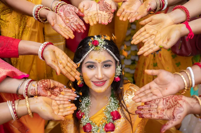 Bride in yellow with floral jewellery smiling as turmeric-covered hands frame her face
