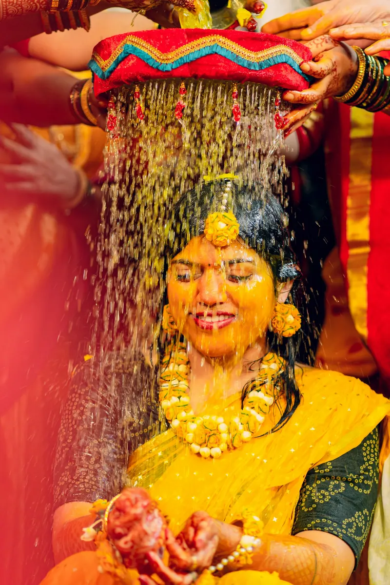 Bride laughing as turmeric water is poured over her from a decorated pot