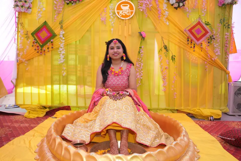 Bride seated in a large decorative urli bowl on a yellow-and-pink haldi stage