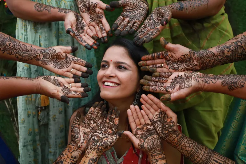 Bride laughing, surrounded by her friends' hennaed hands at the mehendi