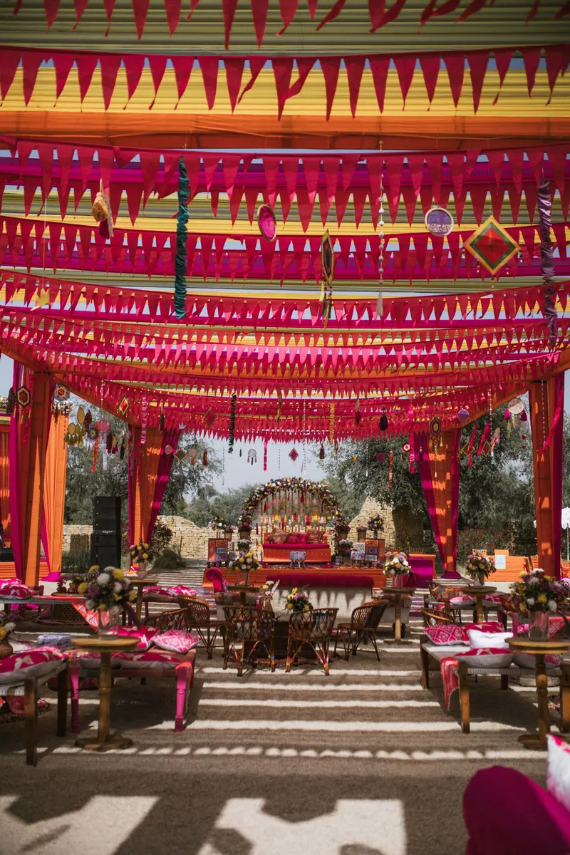 Outdoor mehendi venue under a canopy of pink and orange buntings with floral lounge seating