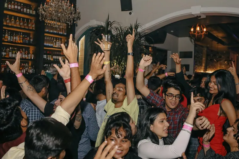 Young Indian crowd dancing with hands raised at a lively night party