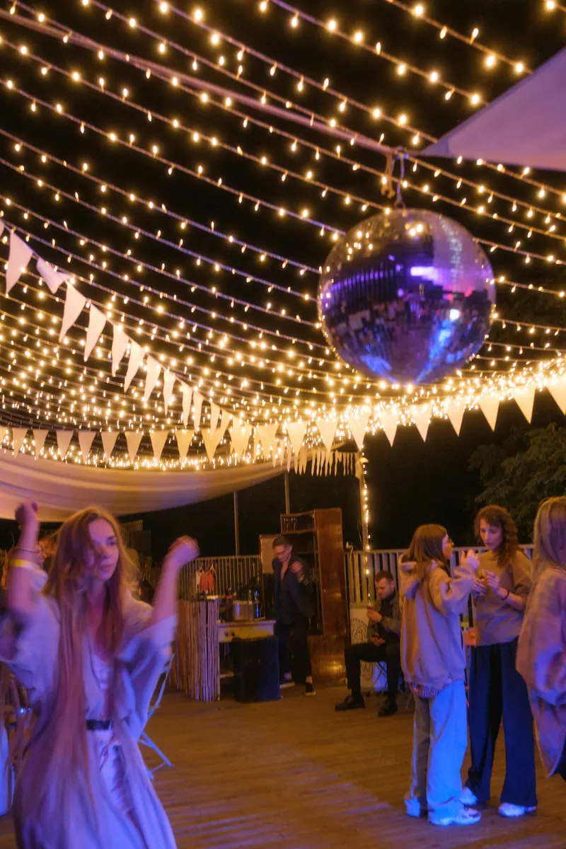 Dancing on a rooftop deck beneath string lights, bunting and a disco ball