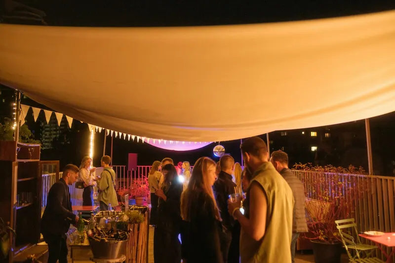 Guests mingling on a rooftop terrace under a lit canopy at night