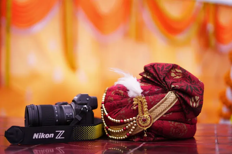 Mirrorless camera beside a groom's embroidered safa against orange decor