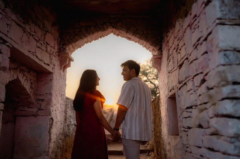 Couple holding hands beneath a weathered stone archway at sunset