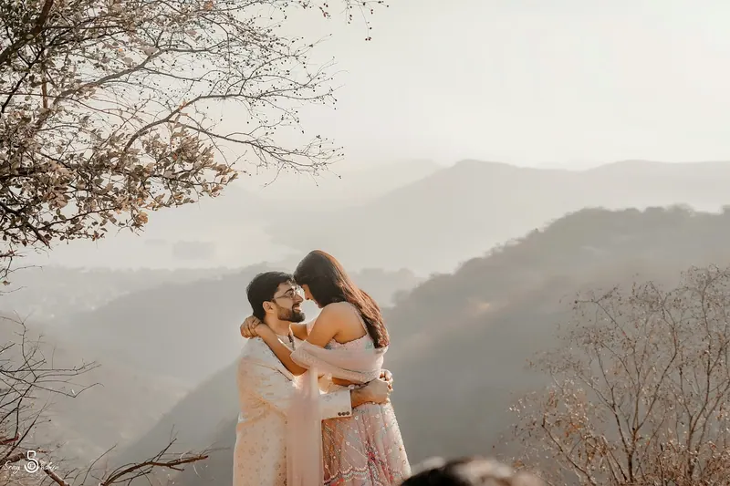 Couple embracing on a hilltop with layers of misty mountains behind them