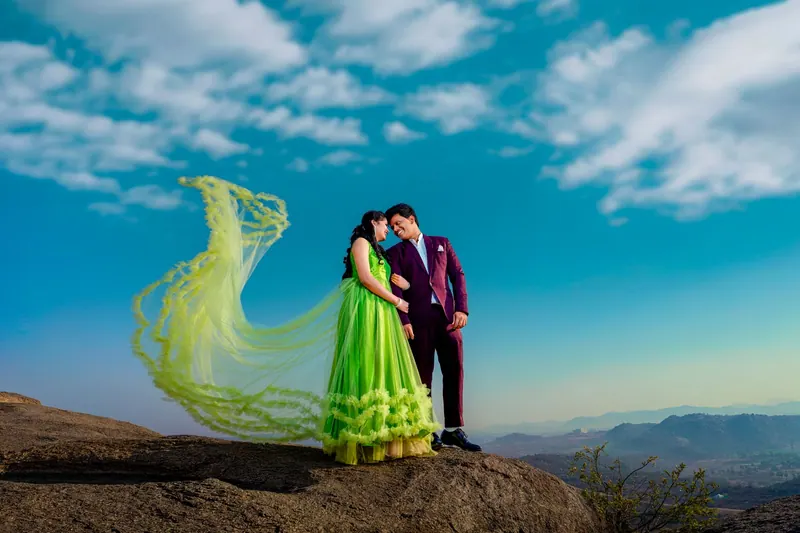 Couple on a rocky mountain top as the bride's flowing green lehenga catches the wind under a blue sky