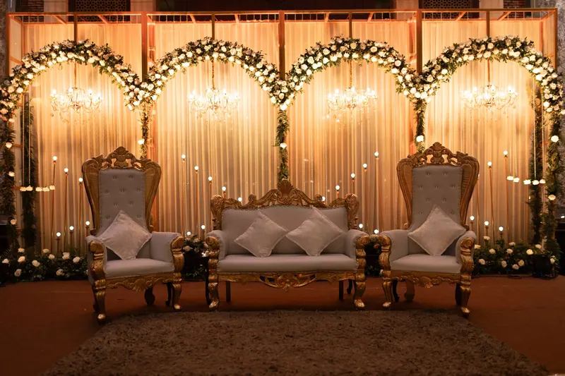 Elegant reception stage with carved gold chairs and a sofa beneath glowing floral arches