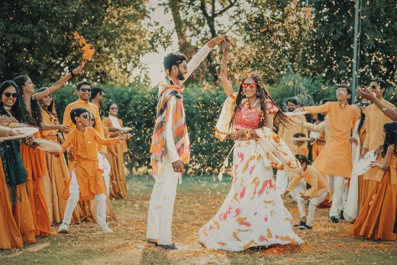 Couple dancing with family and friends in a leafy garden, everyone dressed in colourful festive wear