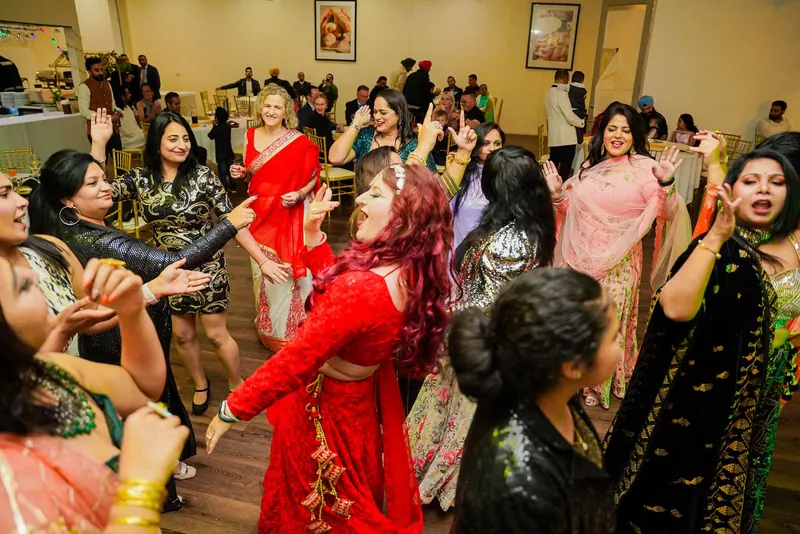 Women in saris and lehengas dancing together at an indoor sangeet