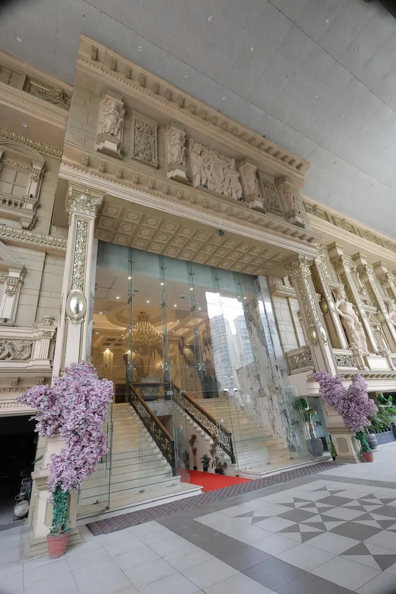 Carved stone entrance with a glass-fronted staircase flanked by lilac blossom trees