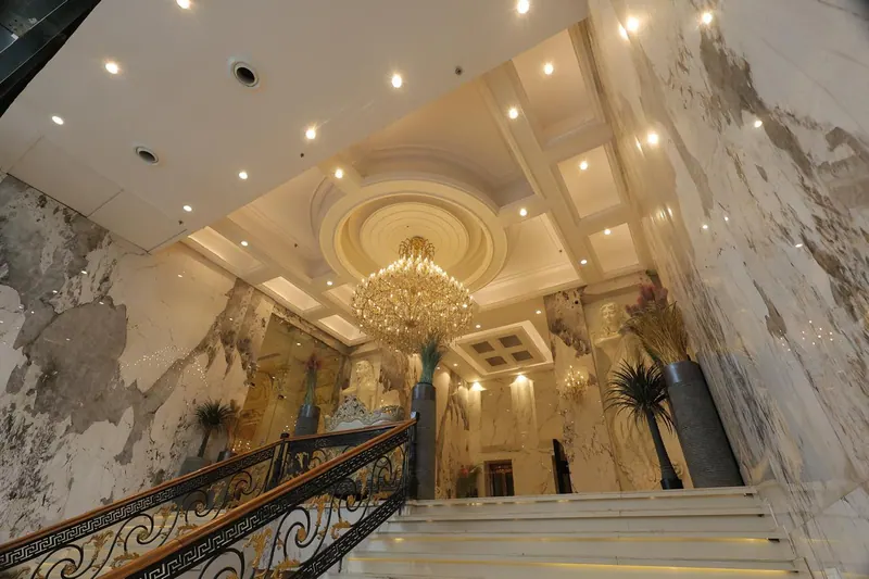 Marble lobby staircase with a wrought-iron rail beneath a crystal chandelier