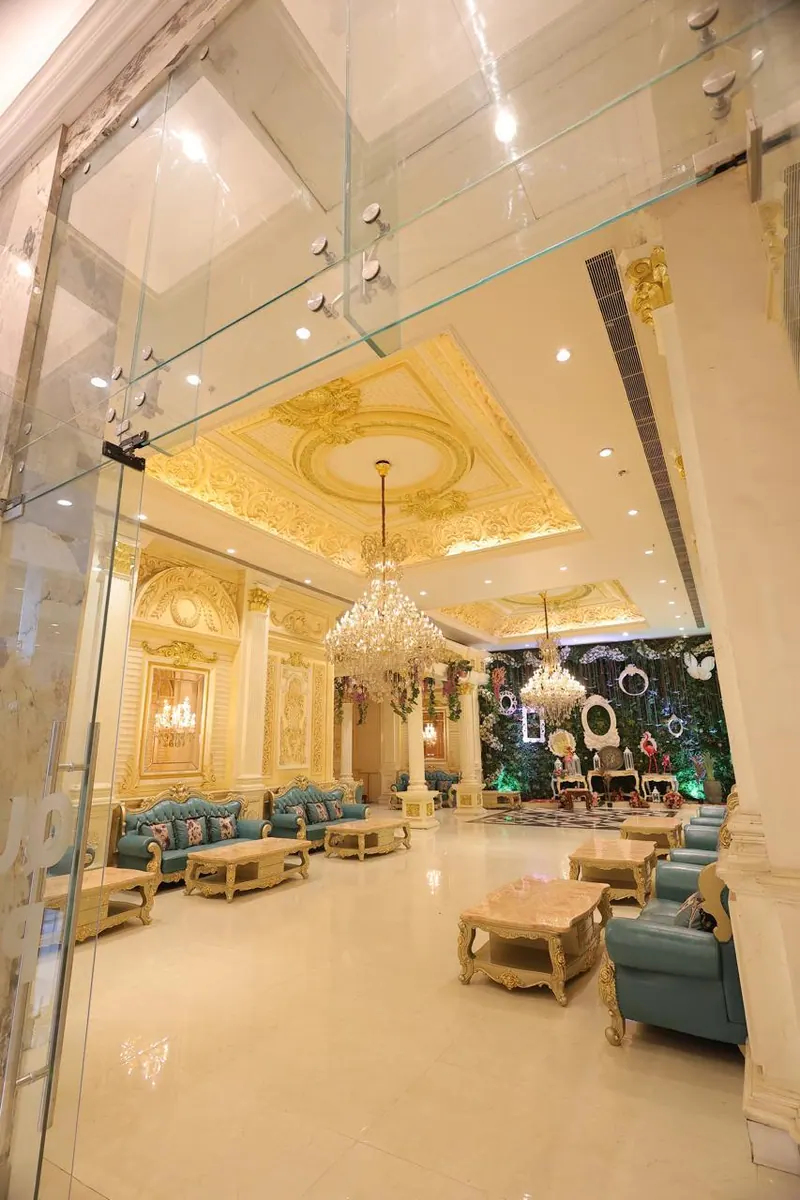 Gilded lounge seen through glass doors, with teal sofas and a crystal chandelier
