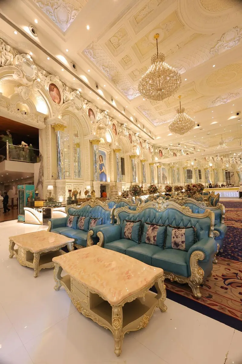 Teal tufted sofas and carved coffee tables in a chandelier-lit hall