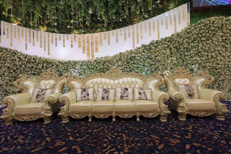 Ivory and gold stage sofas set against a wall of white roses and cascading greenery