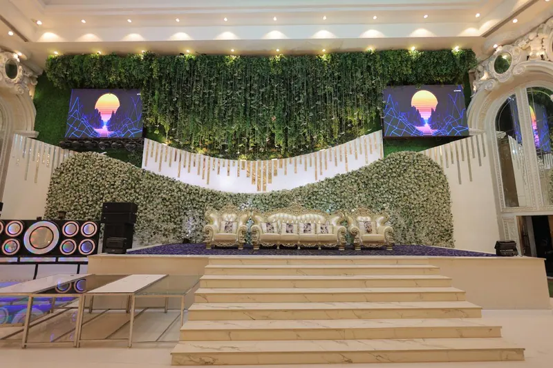 Stage steps rising to a floral wall with hanging greenery and twin LED screens