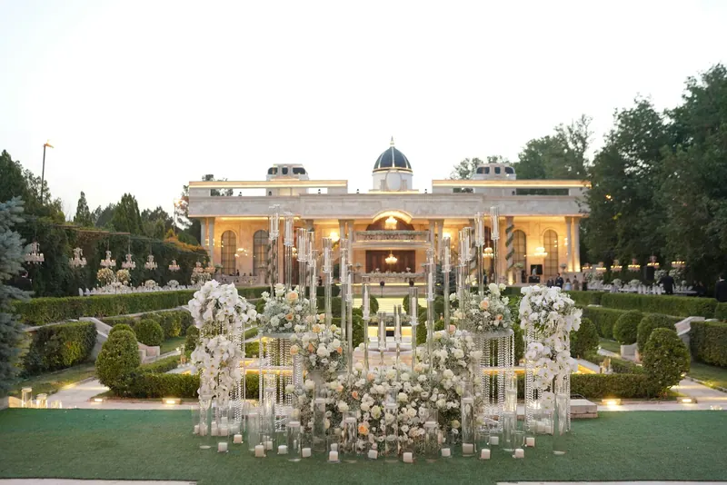 Formal garden before a lit mansion, dressed with white florals and tall glass candle pillars