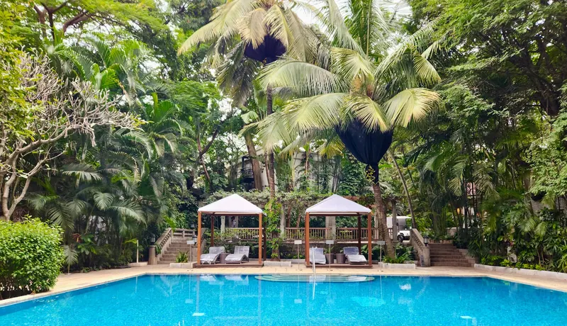 Resort swimming pool framed by palms with white poolside cabanas
